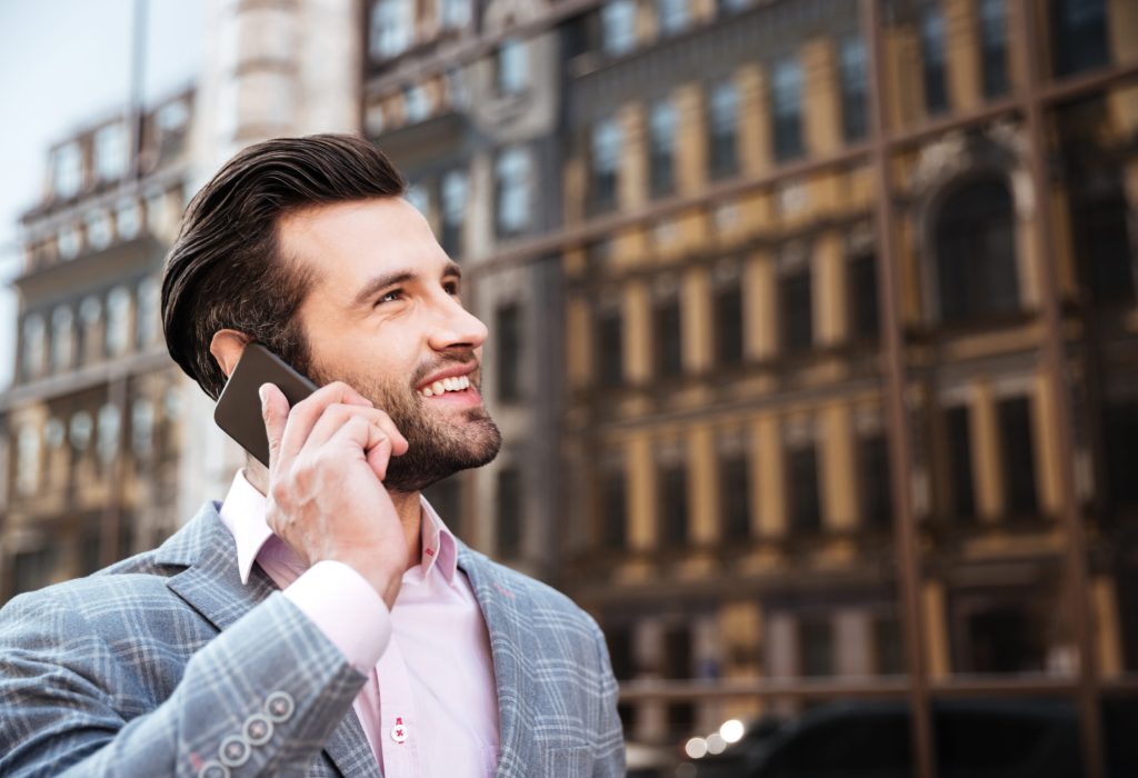 Close up portrait of an attractive bearded man in jacket talking on mobile phone in a city area